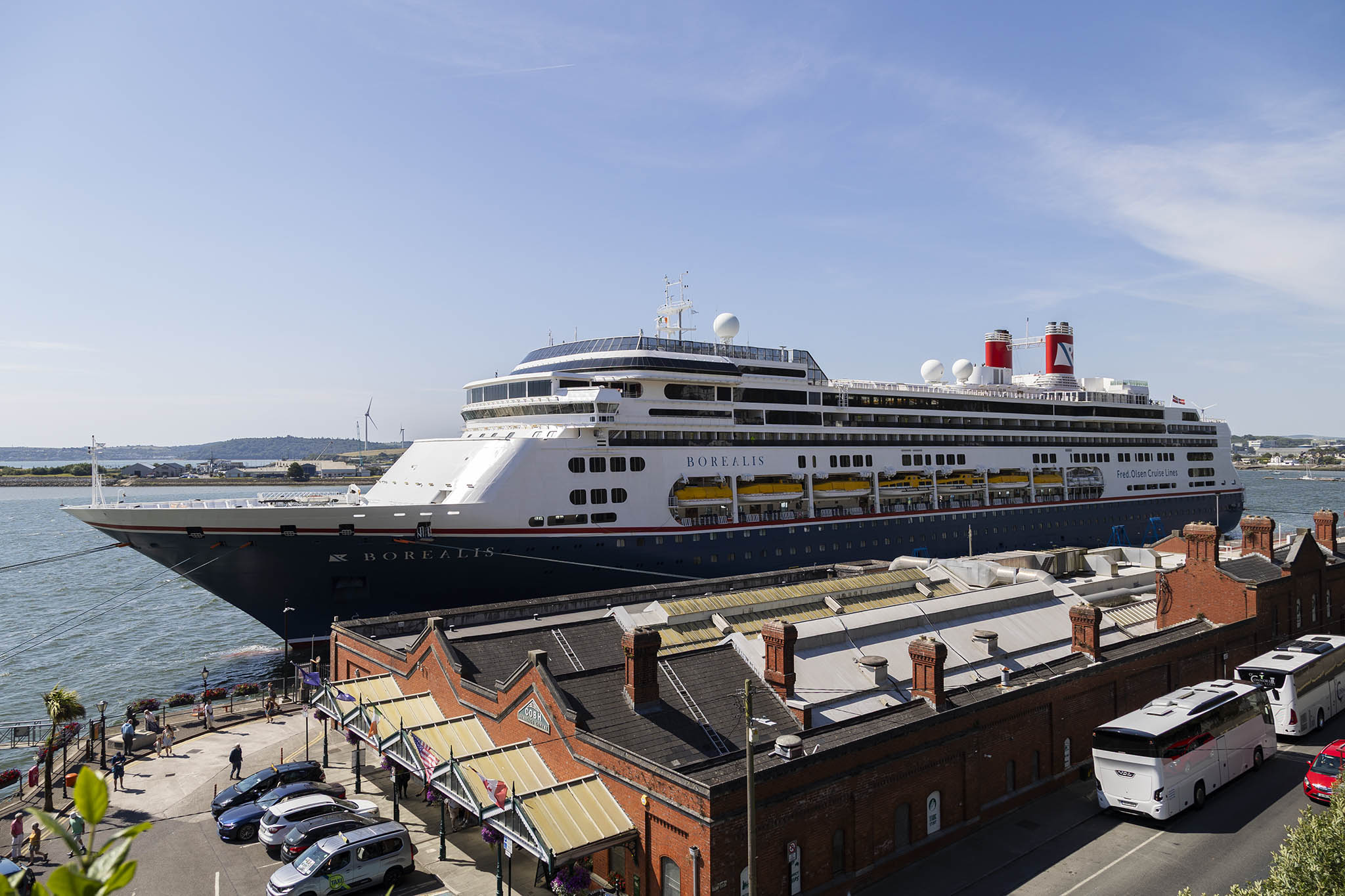 A view from a small hill overlooking a small port area. Docked behind a brick, former-train terminus building there's the Borealis cruise ship.